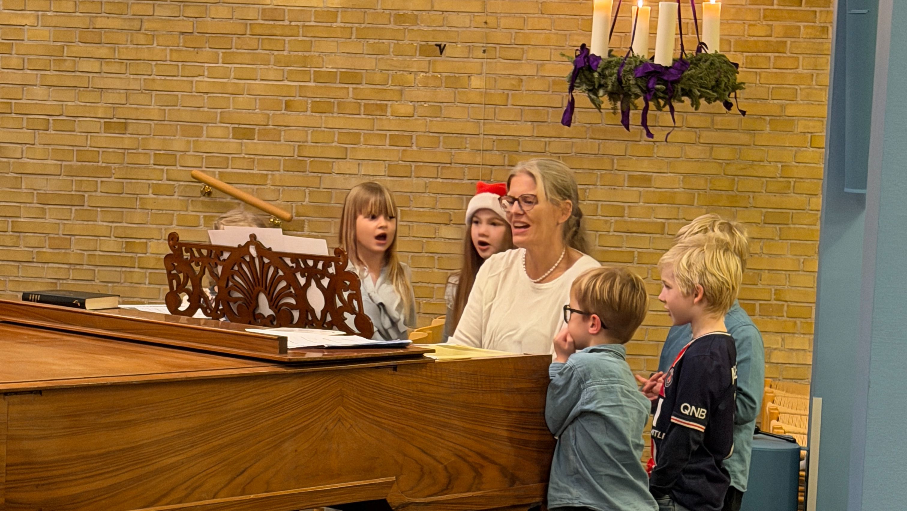 En kvinde og børn synger ved et klaver i en kirke.